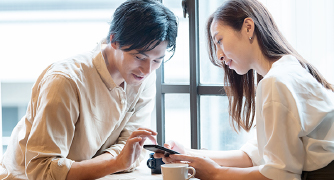 画像:男女が窓際でスマートフォンを見ている様子